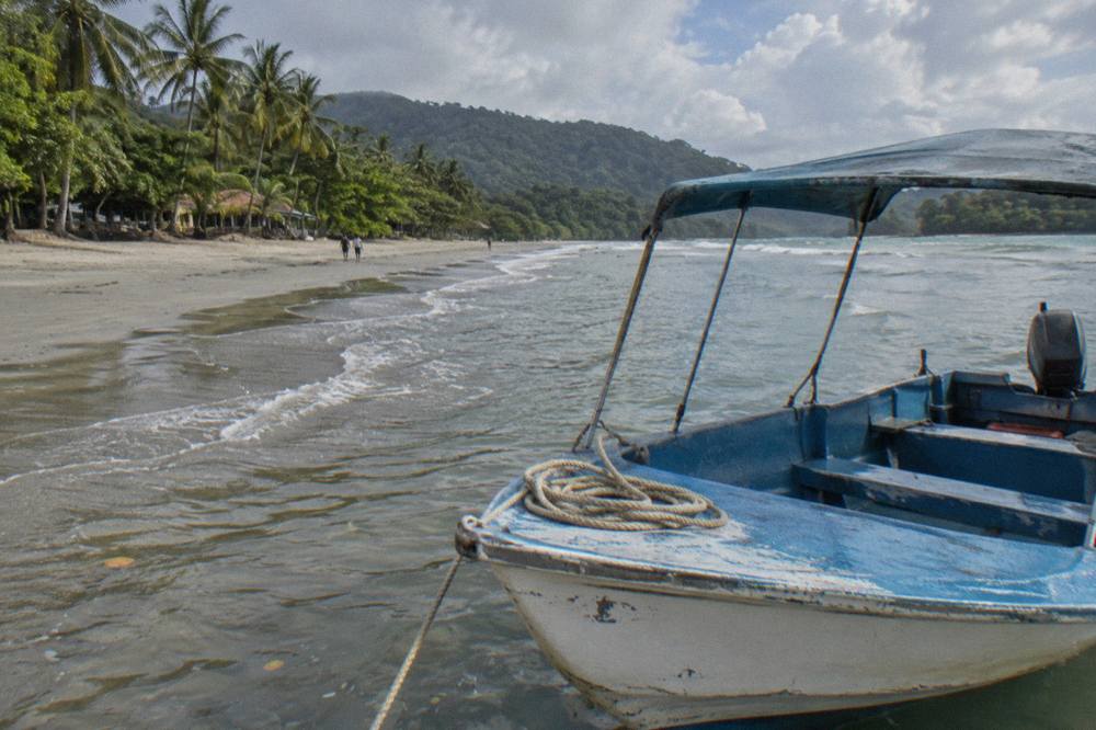 Small open tour boat resting on wet sand beside calm shallows at a tropical beach