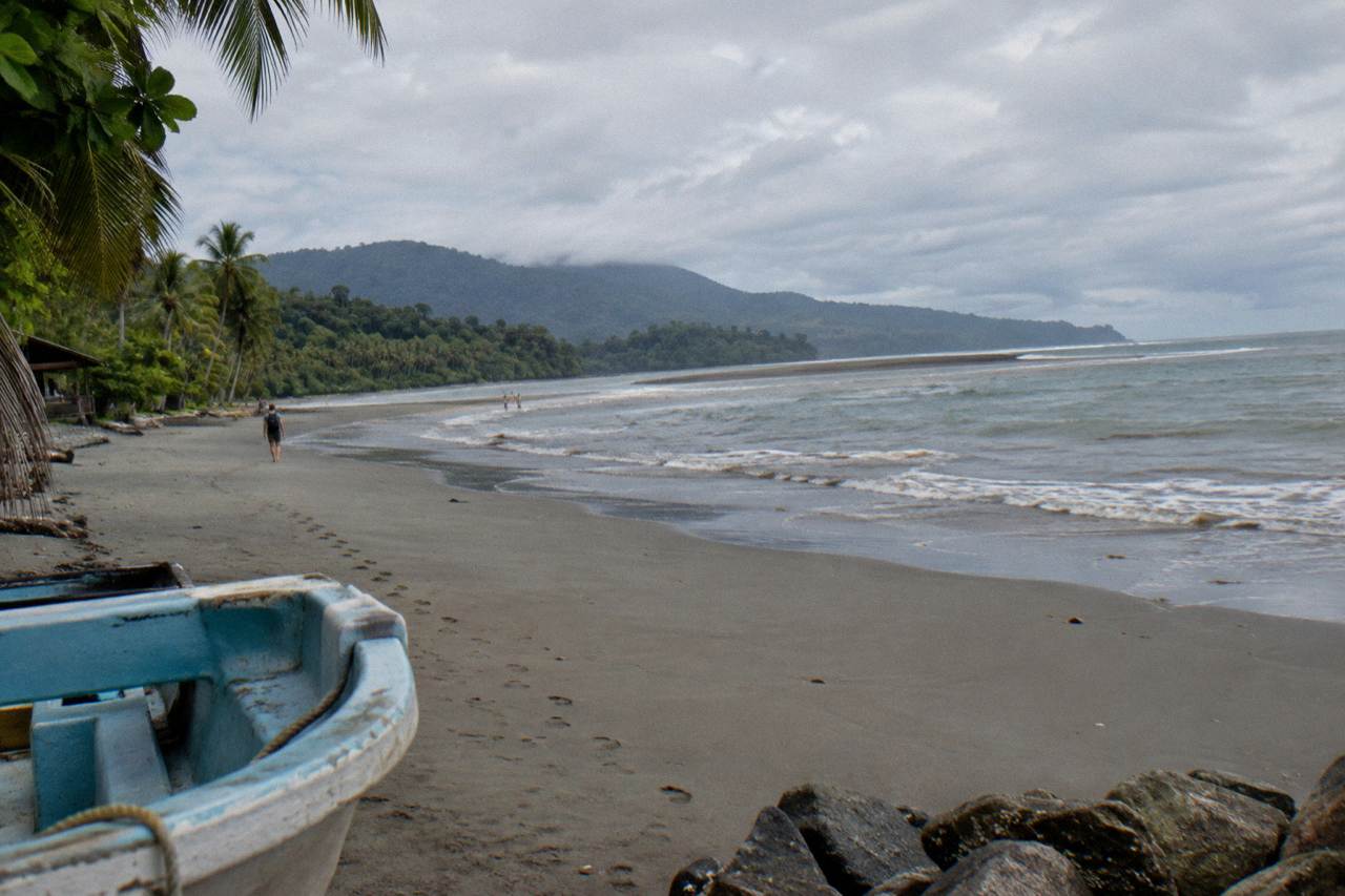 Wide sandy beach curving into a whale tail shaped sandbar under an overcast Pacific sky