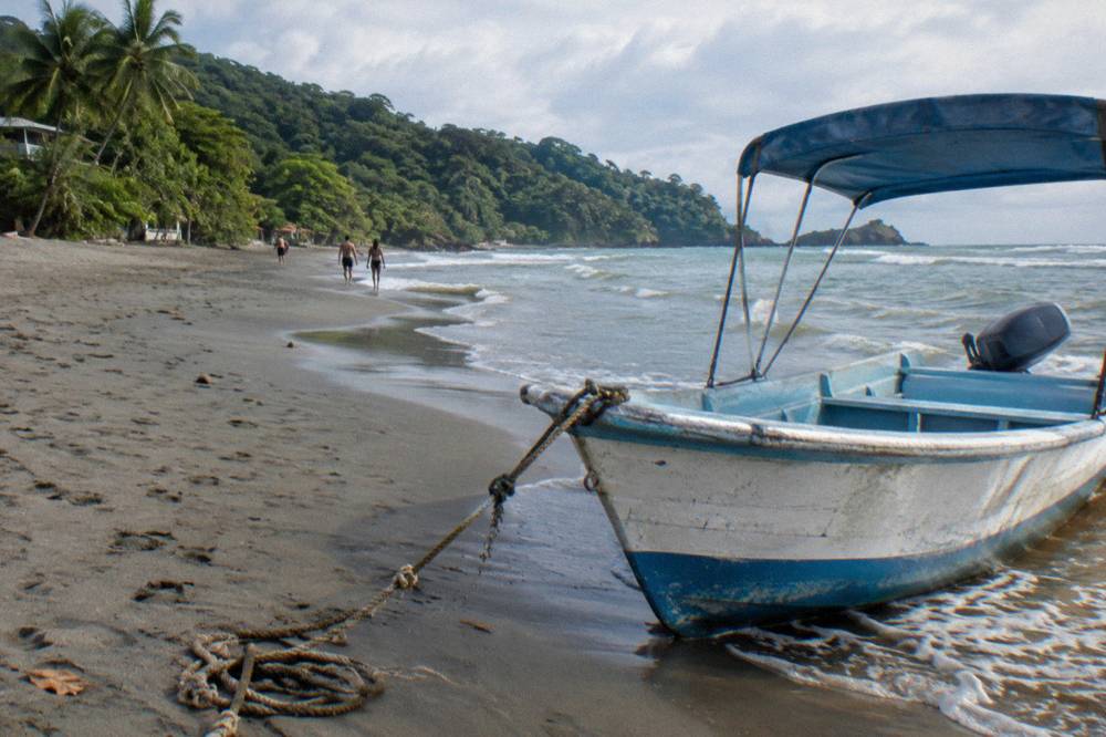 A small open tour boat resting on a wide sandy beach beside gentle waves