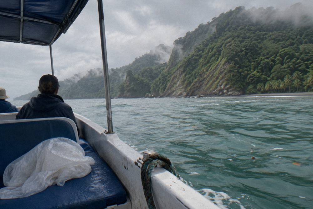 A small open tour boat cruising across a calm turquoise bay toward green headlands.