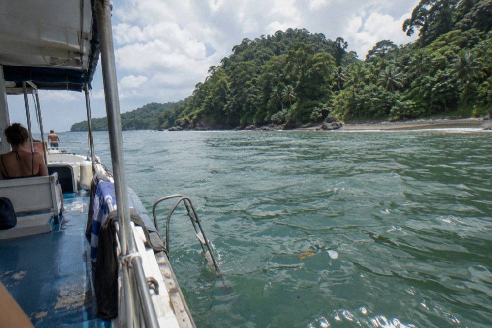 Tour boat at anchor in a calm bay with green forested headlands under a partly cloudy sky