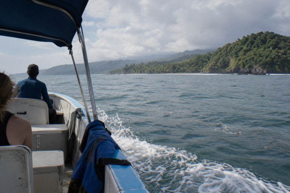 A small open tour boat heading out across a calm bay toward green headlands