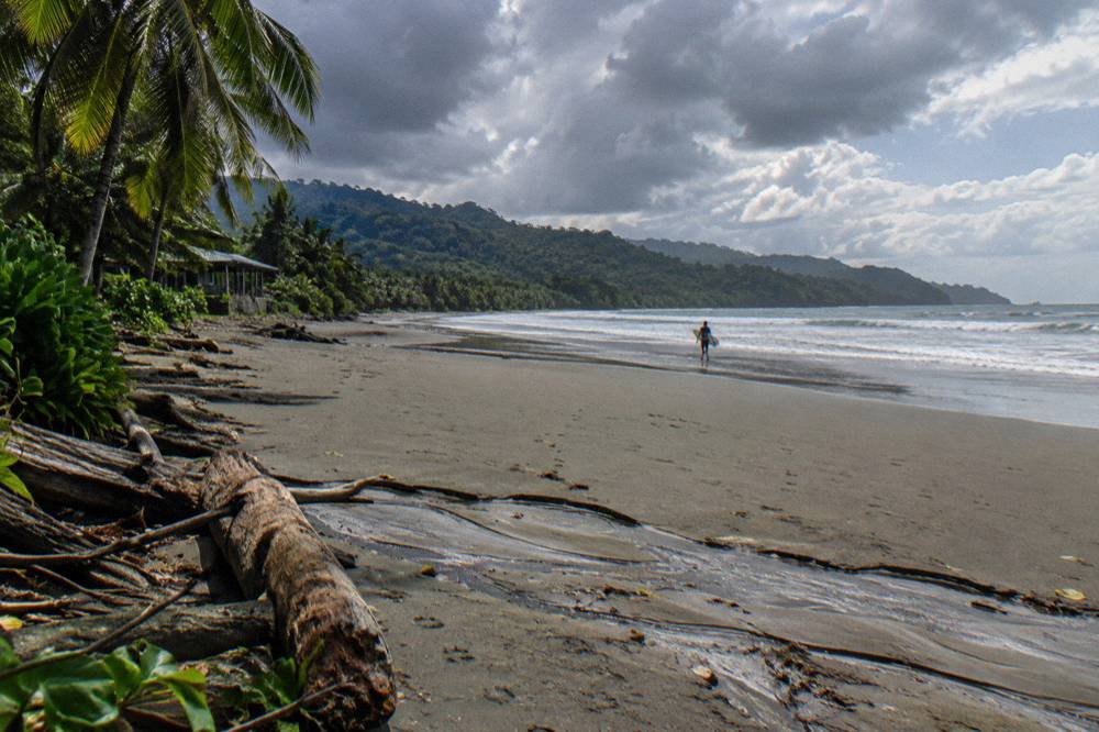 Dark rain clouds over green coastal hills above a wide empty beach