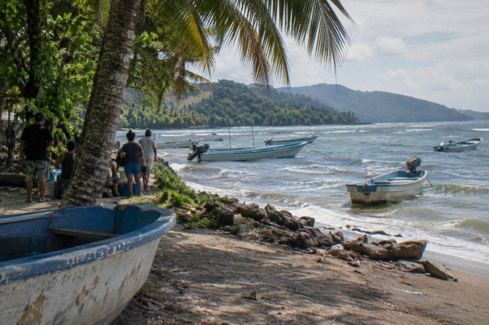 Locals in the shade of palms beside pangas moored off a beach in Bahía Ballena