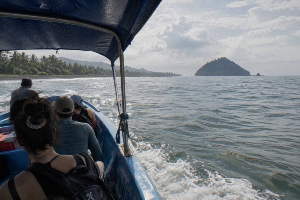 Open boat crossing calm blue water toward a small forested island on the horizon