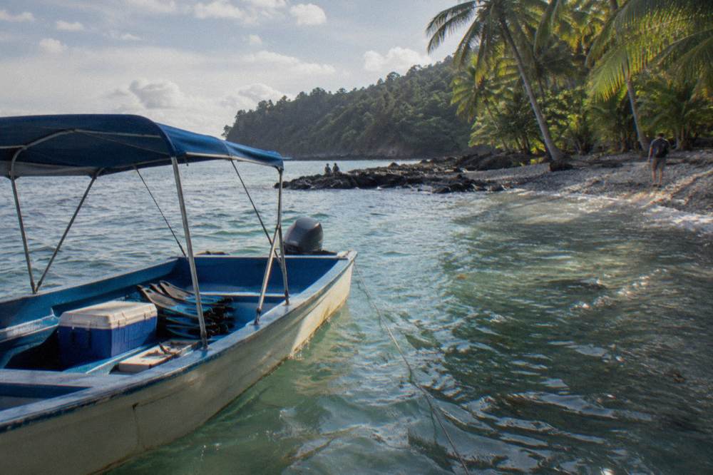 Tour boat anchored near a rocky island shoreline with palm forest and clear turquoise water