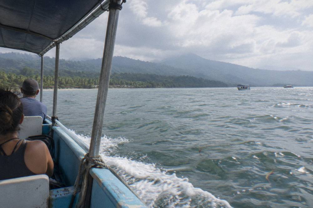 A small covered tour boat crossing a wide bay under morning light