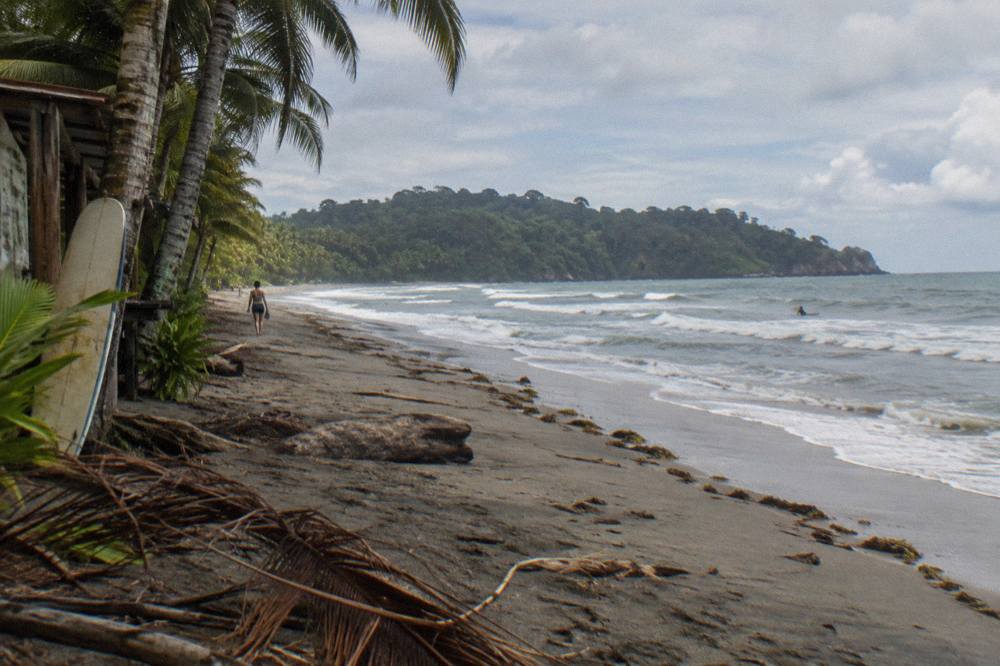Long empty beach curving toward a forested headland under scattered clouds