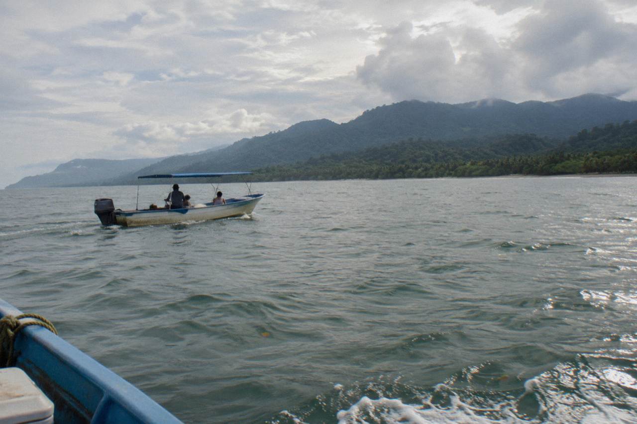 A small open tour boat on calm Pacific water near forested hills