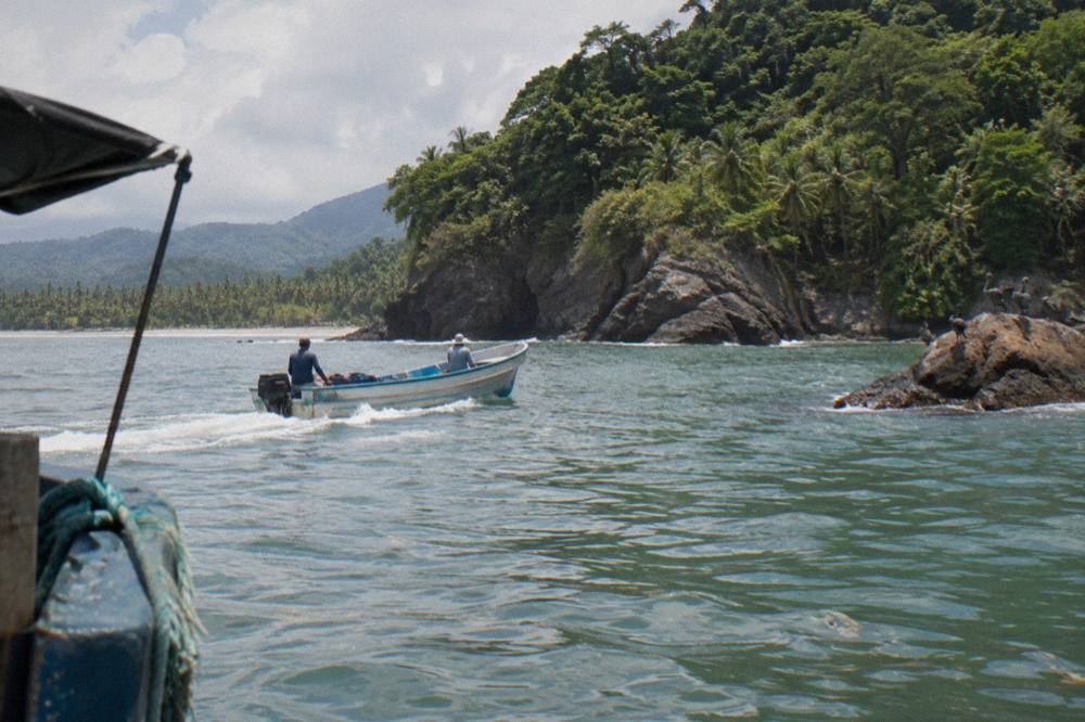 Small boat crossing calm Pacific water near a forested Osa headland