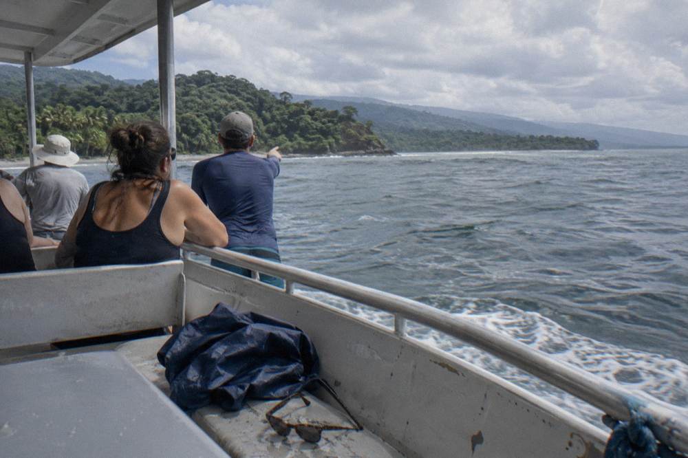 Passengers leaning on a boat rail watching open water with distant hills