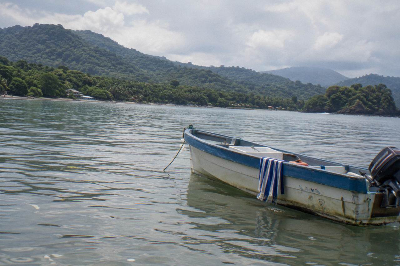 Small boat on calm Pacific water near forested hills at Uvita