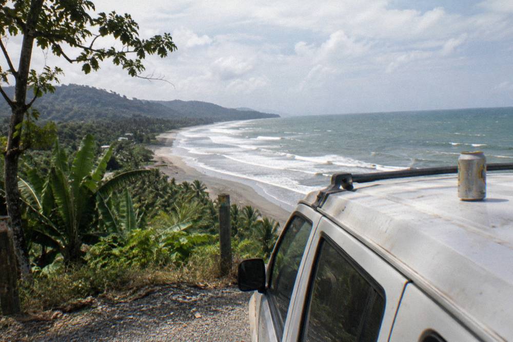 A rental car parked at a coastal viewpoint overlooking a long beach