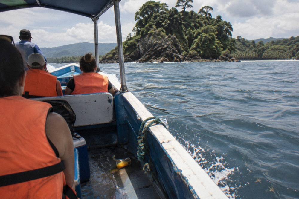 Small open tour boat with passengers in life jackets near a rocky island coastline