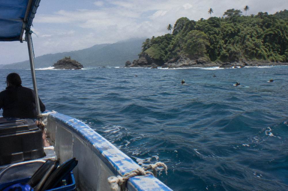 Boat anchored near a forested island with clear deep blue water and rocky islets