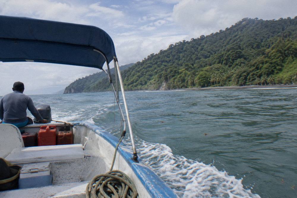 A boat on calm Pacific water near a green forested coastline