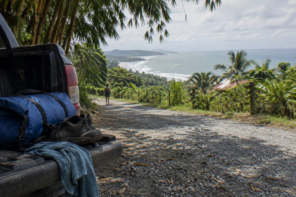 A dry bag and hiking shoes on a truck tailgate beside a rainforest road