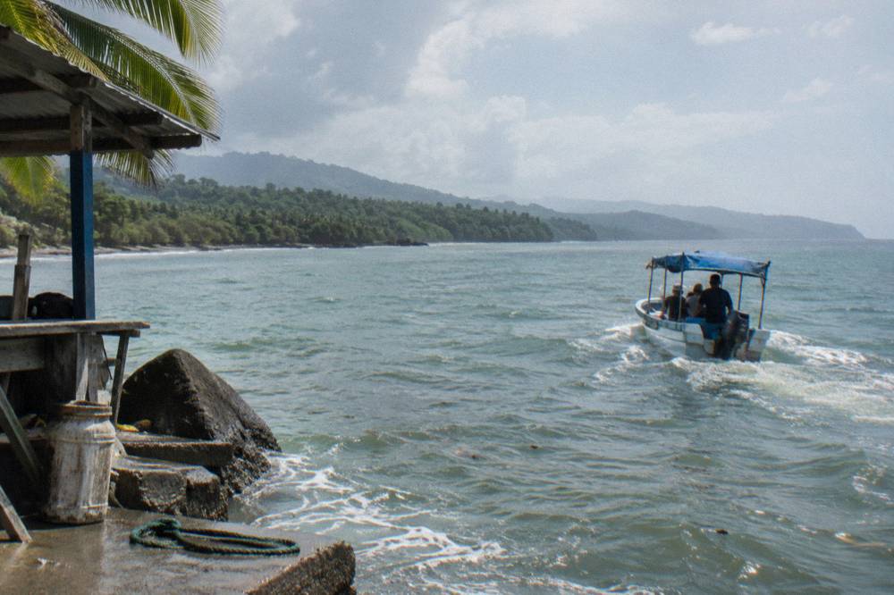 A small open tour boat heading out across green ocean water toward distant hills