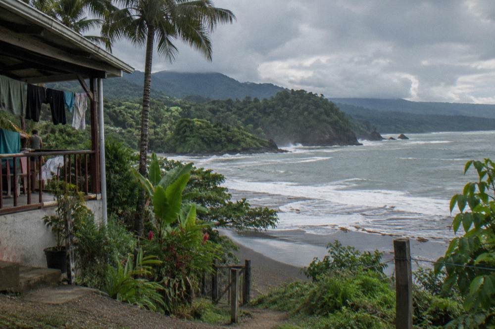Dark rain clouds over forested coastal hills above a grey ocean