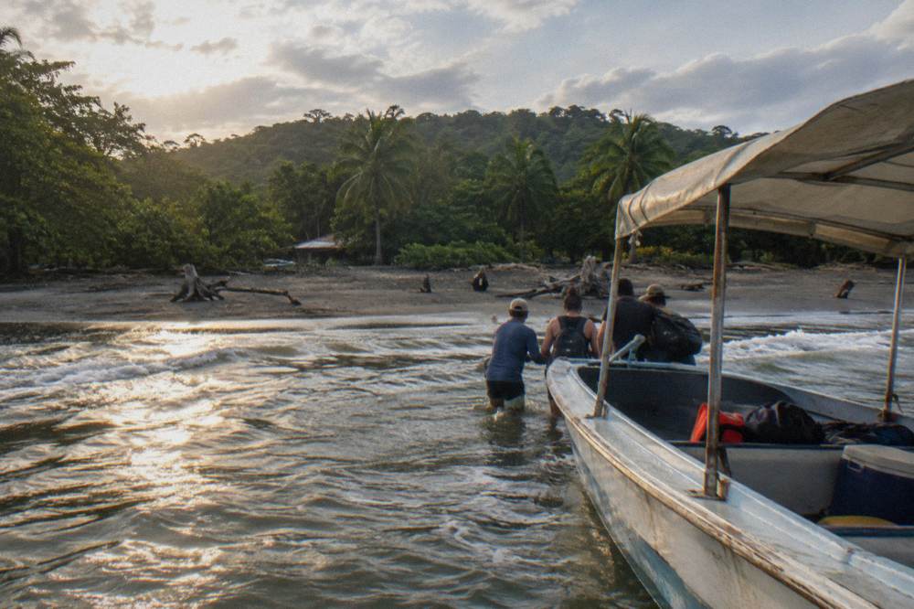 A small open tour boat heading out from a sandy beach into open water