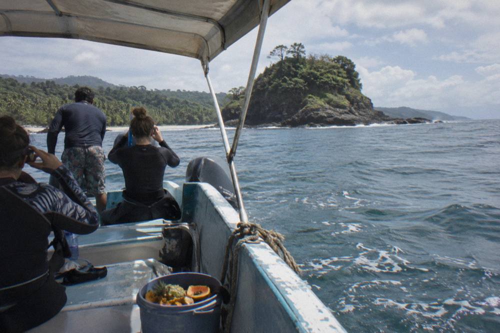 A small tour boat anchored near a rocky island shoreline with passengers preparing to enter the water