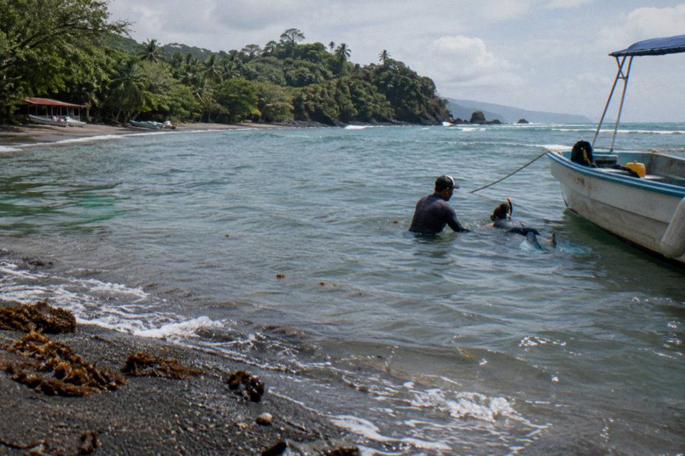Snorkelers and a guide in the water beside a moored boat in a calm bay