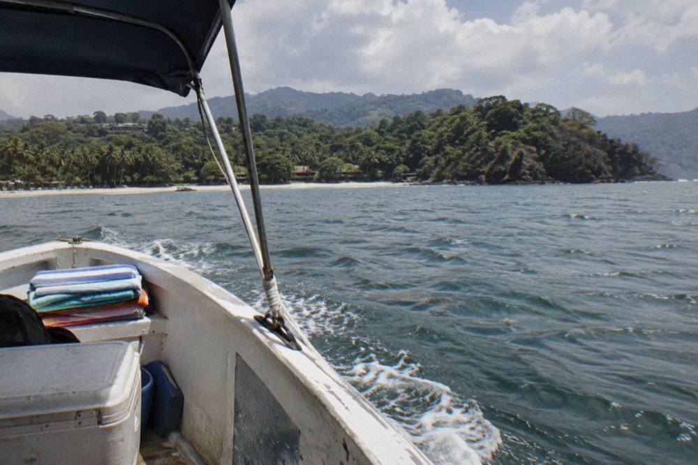 A small open tour boat cruising across a wide calm bay toward green headlands