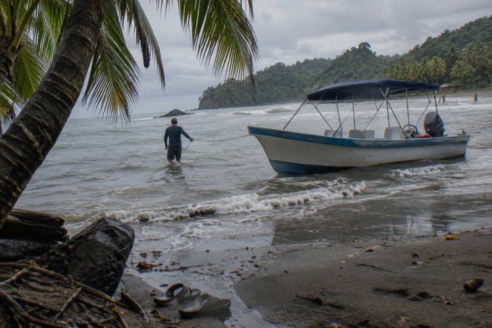 An open tour boat resting on wet sand at the waterline of a tropical beach beside green forest