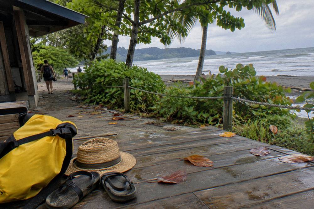 Sandals, a dry bag and a sun hat arranged on a wooden bench beside a beach path