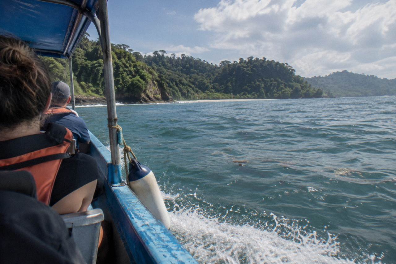 A small open tour boat cruising over calm blue Pacific water near forested hills