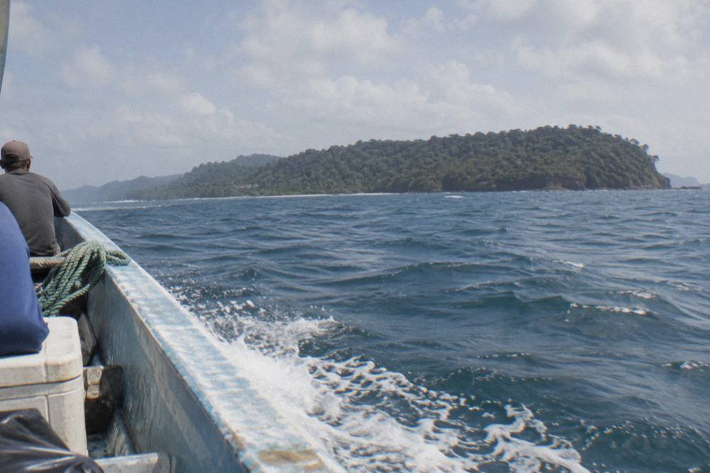 A boat crossing open water toward a distant forested island on the horizon
