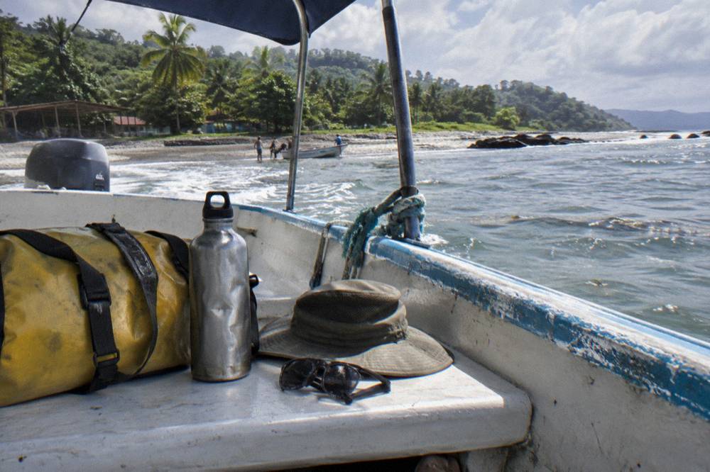 Dry bag and water bottle resting on a boat bench beside a sun hat and sunglasses