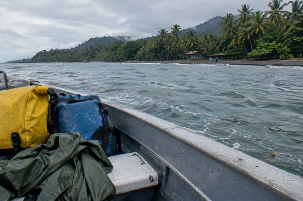 Light rain jacket and dry bags packed on a boat seat under overcast tropical sky