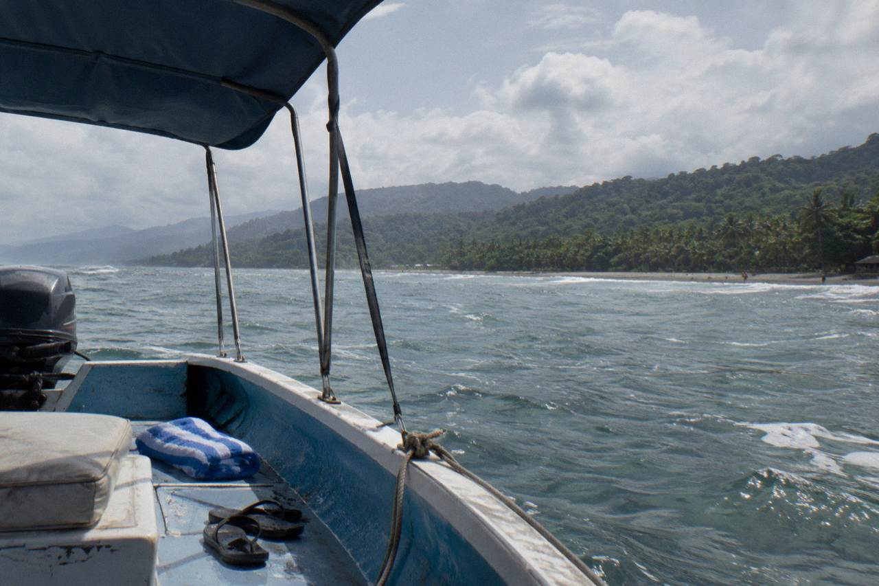 Small open whale watching boat on calm Pacific water near forested hills at Uvita
