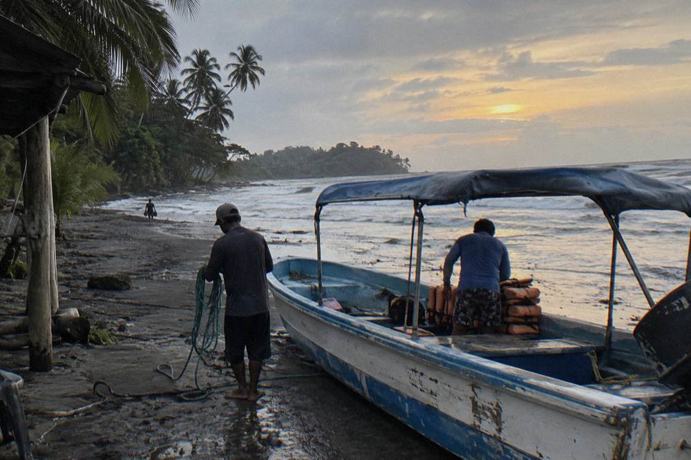 Small boat on the sand at first light with crew preparing gear beside calm Pacific water