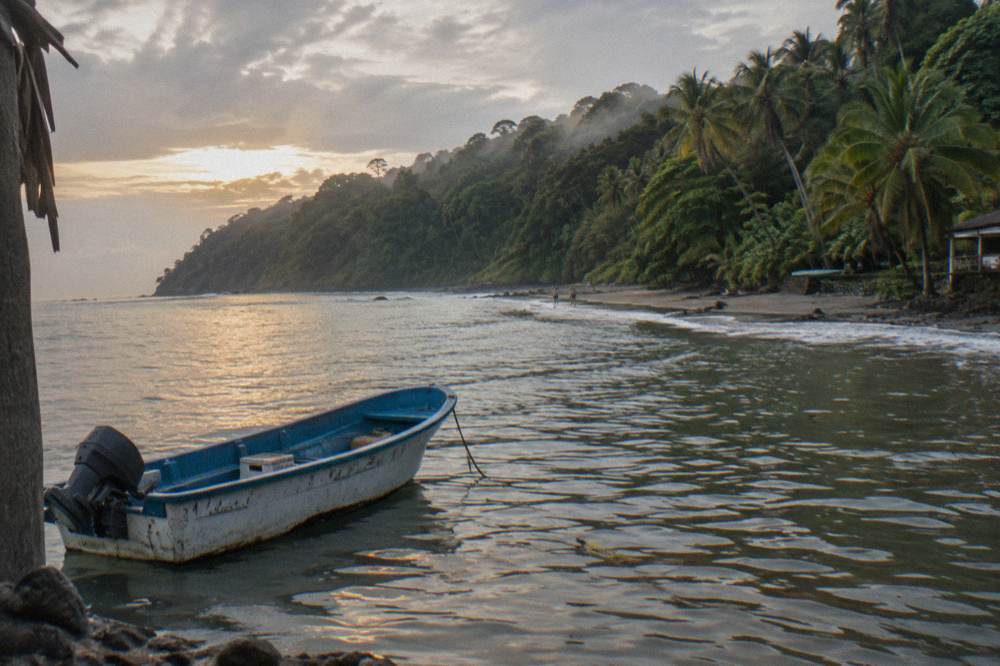 A small boat at anchor in golden morning light close to a wooded shoreline
