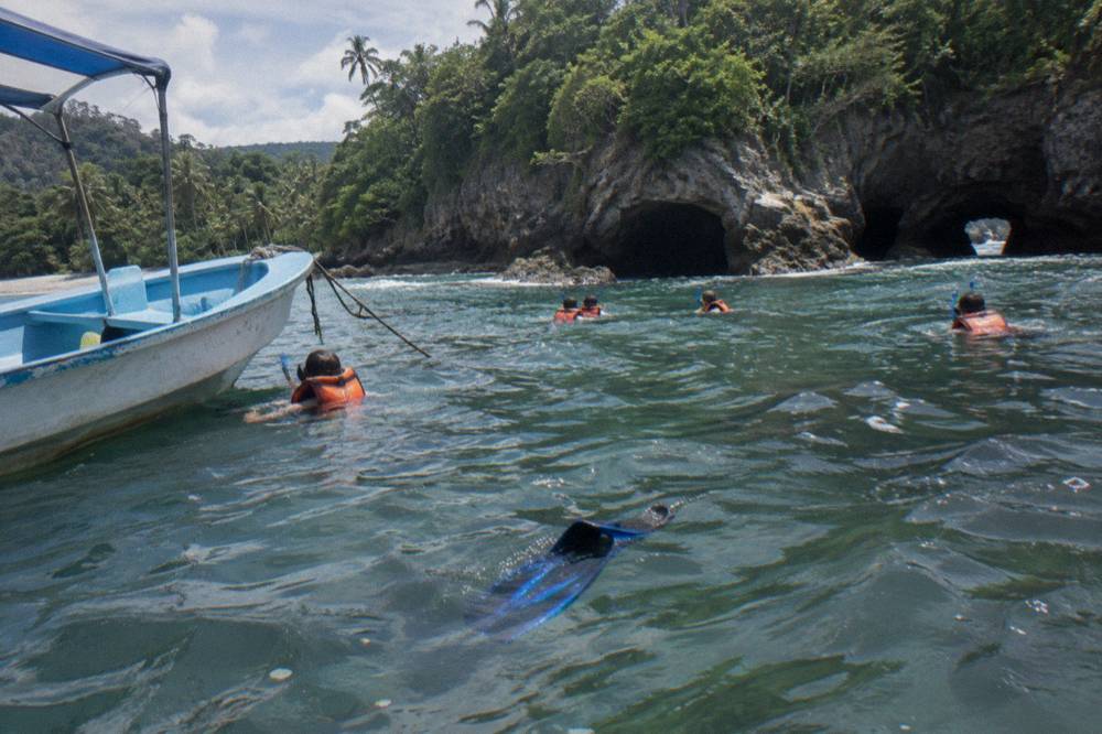 Passengers in life jackets snorkeling in clear water beside a small boat